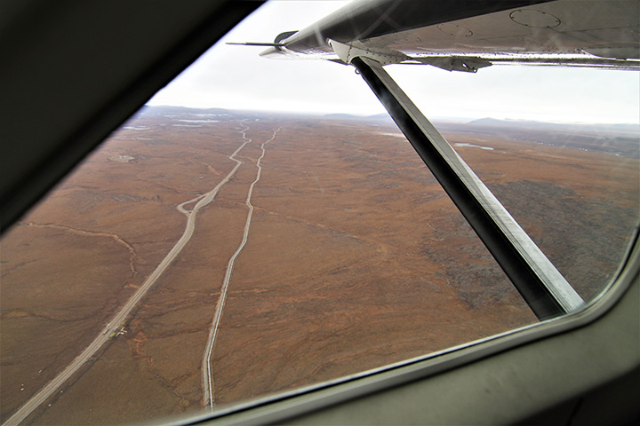 From the passenger seat of a small commuter plane, the Dalton Highway and the Trans Alaska Pipeline are seen running side-by-side north of Atigun Pass
